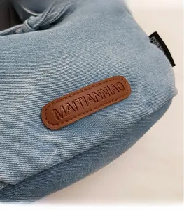 Detail of light blue denim shell bag showing brown leather logo patch and fine stitching