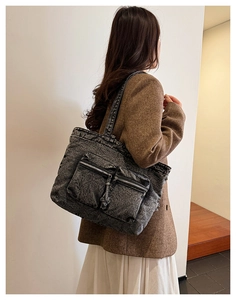 Detail of dark grey washed denim tote bag featuring dual front zipper pockets on a model
