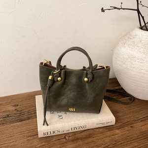 Détail du sac seau vert olive foncé avec clous dorés et poignée nouée sur table en bois
