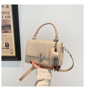Detail of beige crossbody bag featuring herringbone weave and heart wooden bead charm