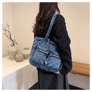 Close-up of acid wash denim tote bag with multiple zipper pockets shown on model