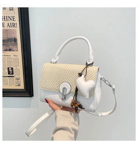 Detail of white leather and straw woven flap handbag with metal lock and heart charm