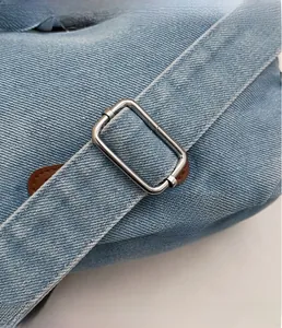 Detail of silver rectangular metal buckle on light blue denim bag with leather trim