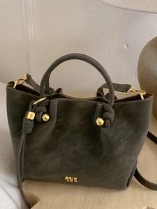 Sac seau rétro en daim vert olive avec détails dorés et poignée sur une table en bois