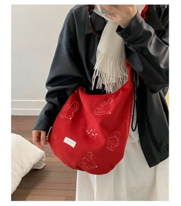 Detail of red canvas crescent bag with white embroidered bird and house patterns