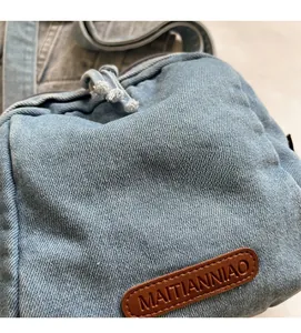 Dettaglio ravvicinato del tessuto denim azzurro e logo in pelle marrone su borsa a guscio