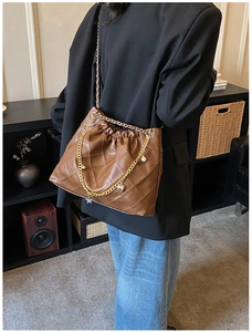 Detail view of brown quilted PU leather shoulder bag with gold chain charms and stitch detail