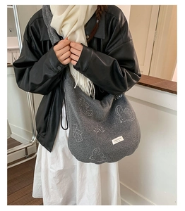 Close-up of dark grey felt tote bag with white embroidery patterns and woven brand label