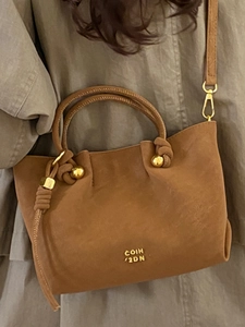 Sac seau vintage marron mat avec poignée nouée et boule dorée sur manteau olive