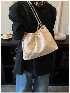 Detail view of beige quilted handbag with gold chain strap and pearl star pendant charms