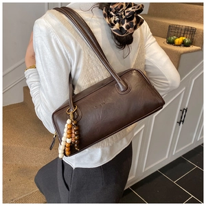 Detail of retro dark brown leather shoulder bag with embossed logo and wooden bead charm