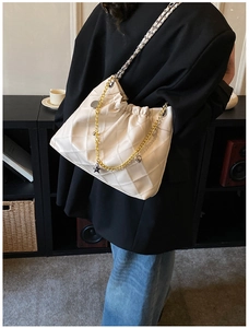 Detail of cream quilted crossbody bag featuring metal chain strap and charm accents