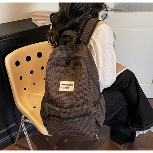 Detail of a brown plaid backpack with a woven brand label and durable canvas material