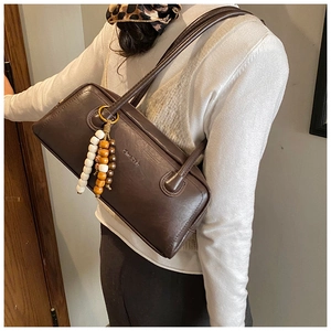 Macro detail of dark brown retro shoulder bag with beaded charm and leather texture