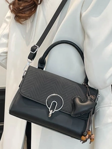 Chic black crossbody bag with herringbone texture and heart pendant on white blazer