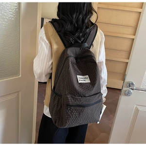Detail of a brown plaid backpack showing the durable fabric texture and side pocket design