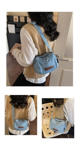 Detail of light blue denim half-moon crossbody bag with dual zippers and leather logo patch