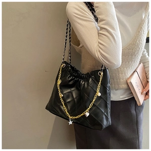 Detail of black quilted shoulder bag with drawstring closure and metal charm chain