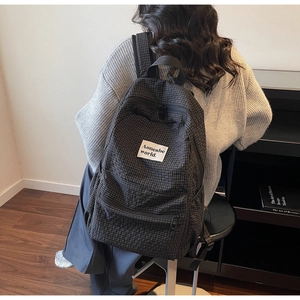 Rear view of a stylish black checkered backpack with brand label worn in a modern room