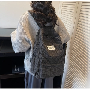 Detail of checkered backpack featuring branded patch and multi-pocket structure
