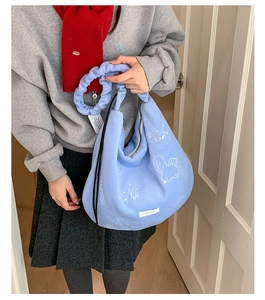 Close-up of light blue plush tote bag with white floral embroidery and ruched strap