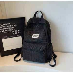 Detail view of black plaid backpack featuring dual zippers and multiple storage pockets