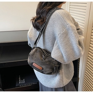 Detail view of a vintage dark grey denim crossbody bag with brown leather patch on model