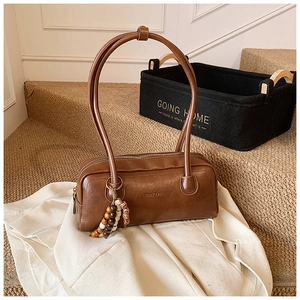 Close-up of brown leather cylinder bag featuring vintage texture and wooden bead tassel