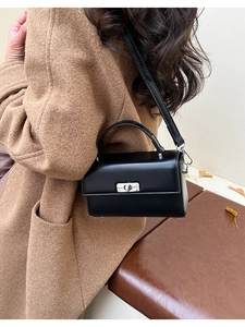 Detail of a structured black crossbody bag with silver twist lock on a camel coat