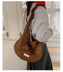 Detailed view of the dark brown suede tote bag featuring white line embroidery and pleated strap