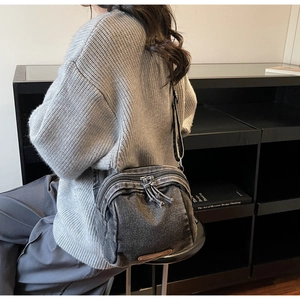 Dettaglio della borsa a conchiglia in denim lavato con doppia zip indossata da una modella