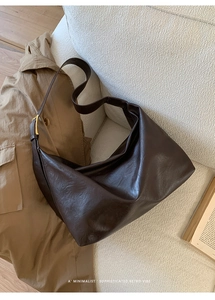 Detail view of large dark brown retro tote bag with smooth texture and metal buckle on sofa