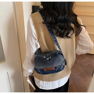 Detail of vintage washed denim crossbody bag featuring premium brown leather brand patch