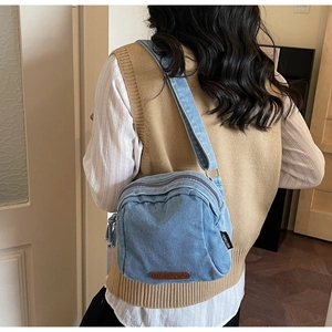 Dettaglio della trama denim e logo in pelle sulla borsa a tracolla azzurra da donna
