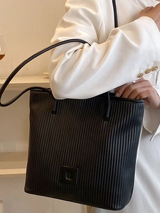 Elegante borsa tote nera plissettata con fibbia quadrata indossata su un completo bianco