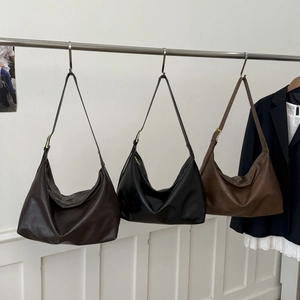Three large crescent hobo bags in dark coffee black and light brown displayed on a rack