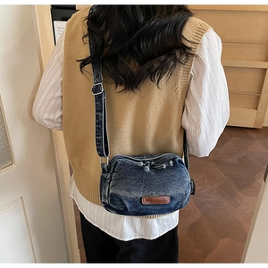 Detail of vintage blue denim crossbody bag featuring a brown leather logo and adjustable strap