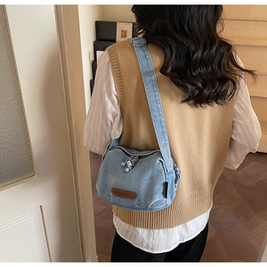 Detailed close-up of light blue denim crossbody bag with brown leather logo tag and wide strap