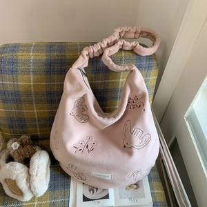Detail view of pink velvet tote bag with bird embroidery and ruched strap on a sofa
