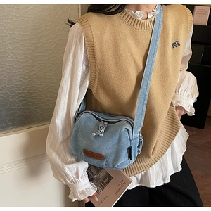 Detail of light blue denim crossbody bag featuring a brown leather logo patch and zipper