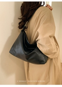 Detail view of large black tote bag with soft leather texture and golden buckle on model