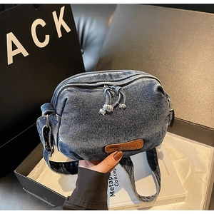 Detail shot of blue denim crossbody bag featuring leather patch and knot zipper puller