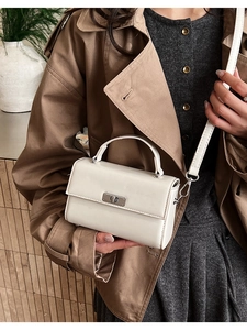 Close-up of white crossbody square bag with silver metal swivel lock on khaki trench coat