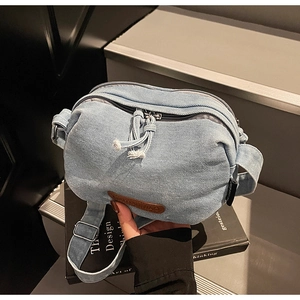Detail of light blue denim crossbody bag with brown leather logo and woven zipper pull