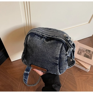 Dettaglio della borsa a tracolla in denim blu con toppa in pelle marrone e tasche con zip