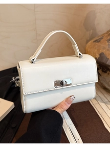 Close-up of a white leather handbag featuring a silver turn-lock and metal protective feet
