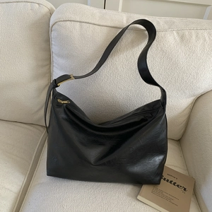 Detail of minimalist black hobo bag with zipper and golden adjustable buckle on sofa