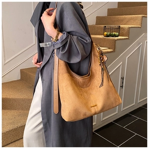 Détail du sac hobo en daim marron caramel avec pendentif à franges sur une bandoulière large