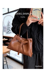 Detail view of caramel brown bucket bag with decorative bow tie on model's wrist