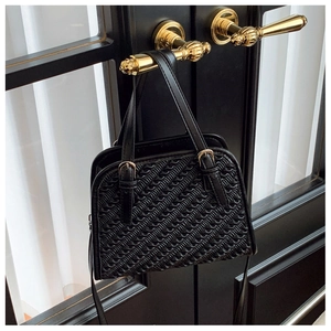 Détail d'un sac à main noir tressé avec ferrures dorées suspendu à une poignée de porte